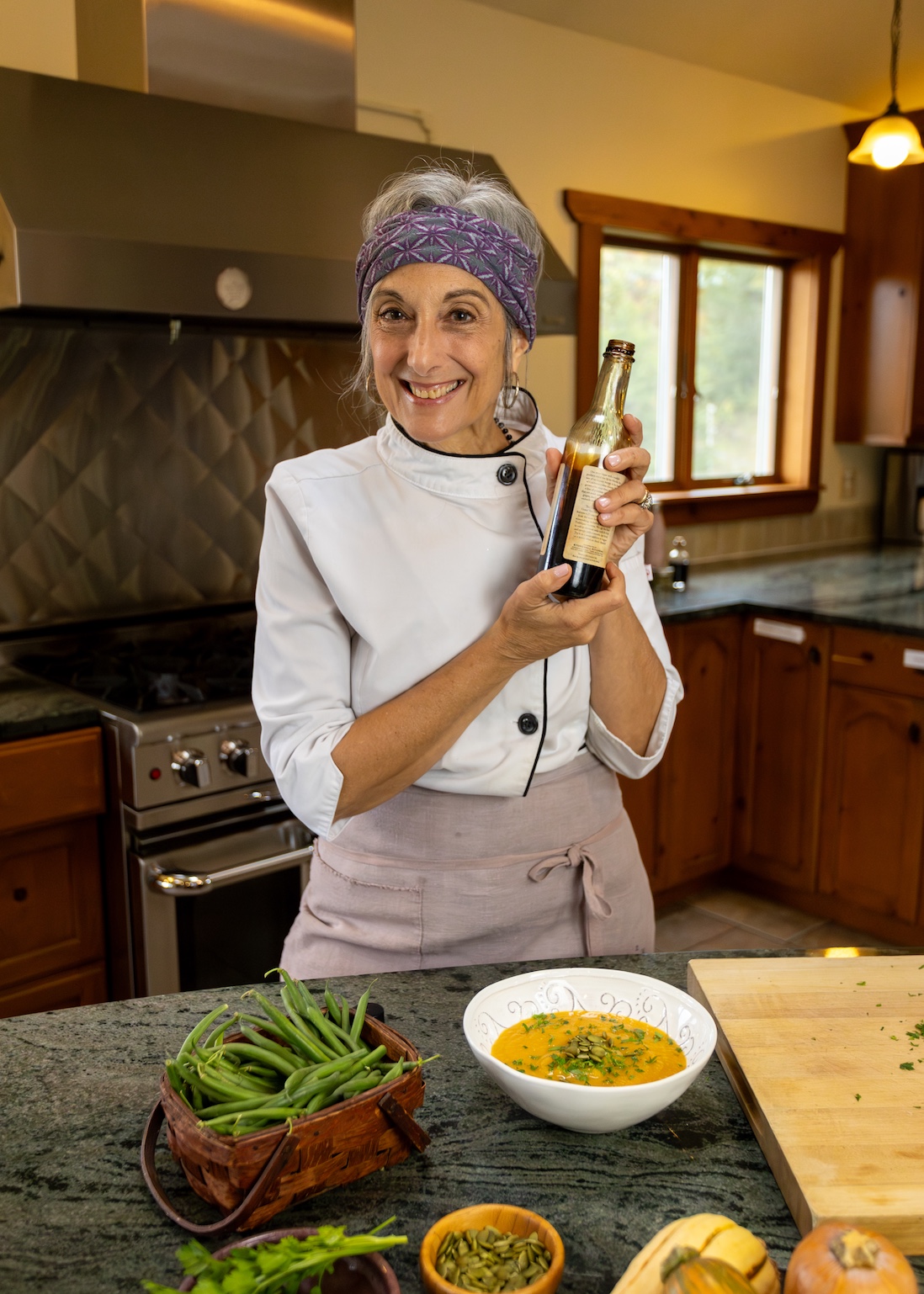 Cathy Vogt in a kitchen wearing a white chef coat holding a bottle of her favorite balsamic glaze