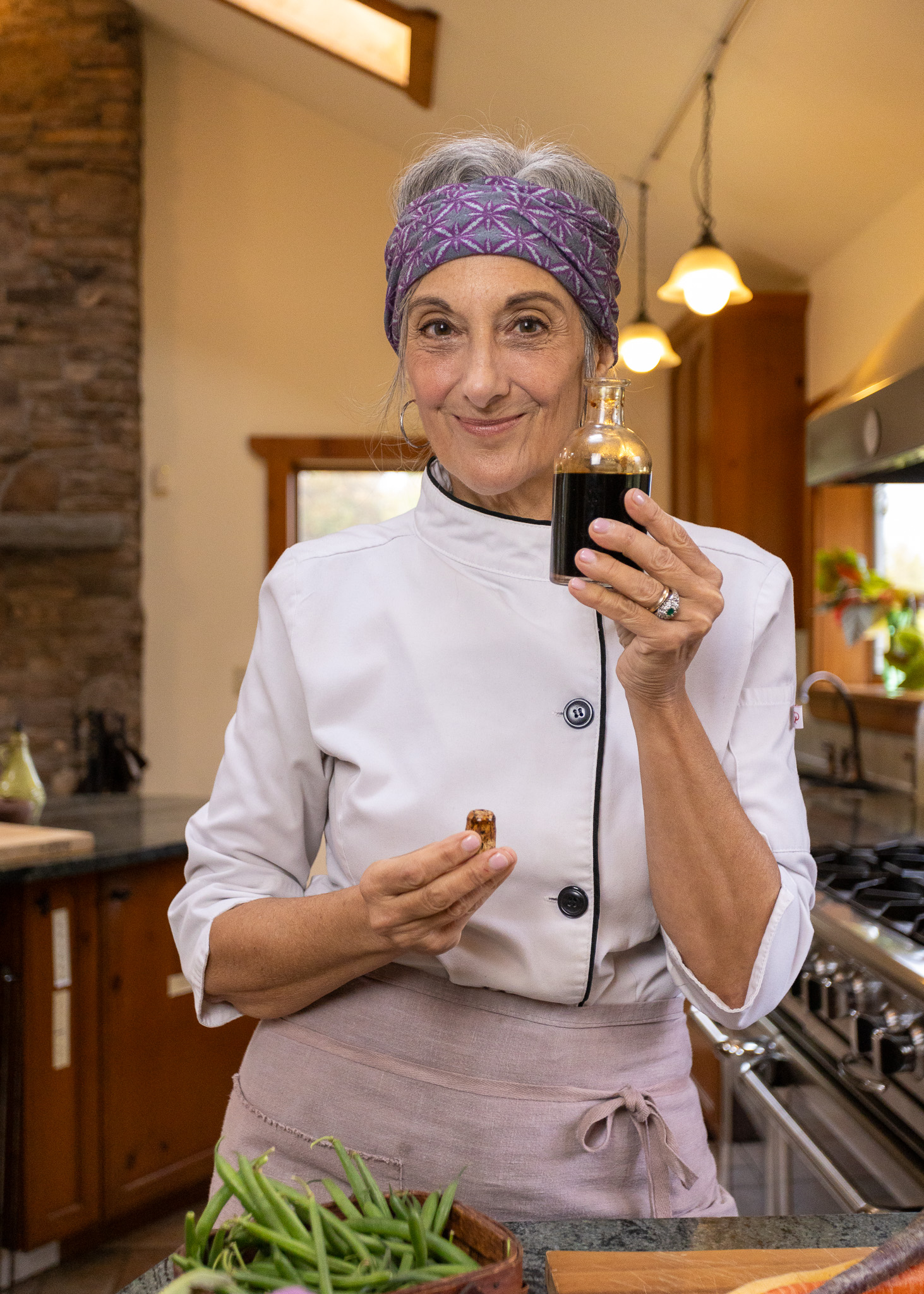 Cathy Vogt personal hudson valley chef holding a bottle in a kitchen while smiling